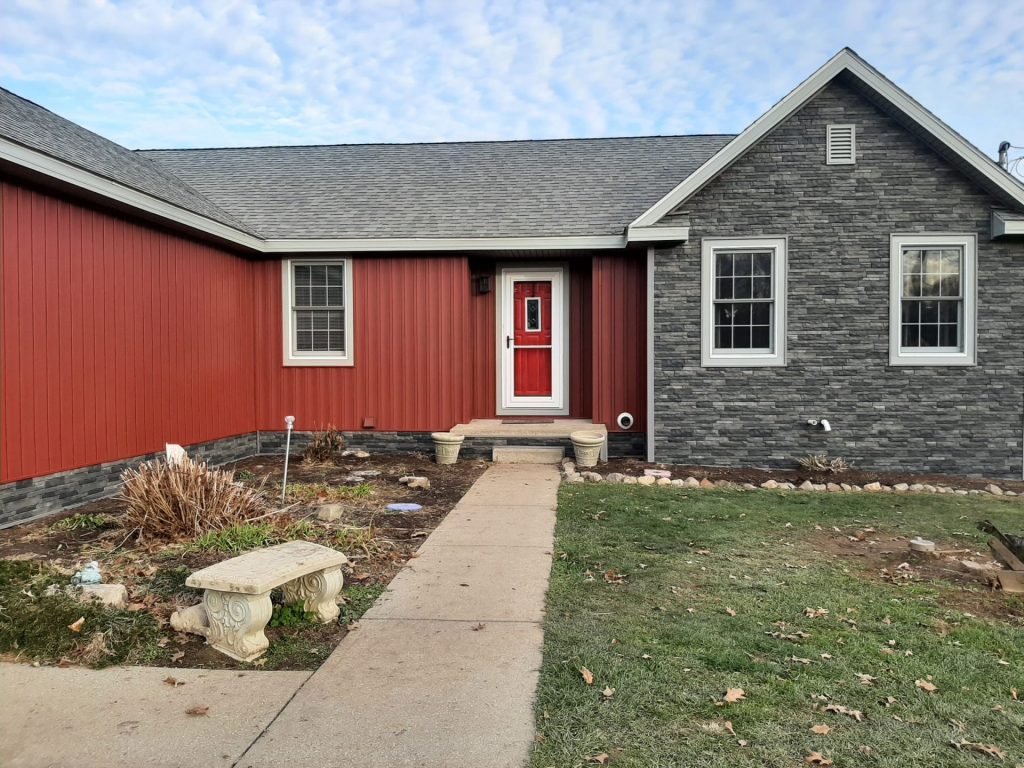 A red house with asphalt roofing, fresh mulch beds, and newly planted shrubs.