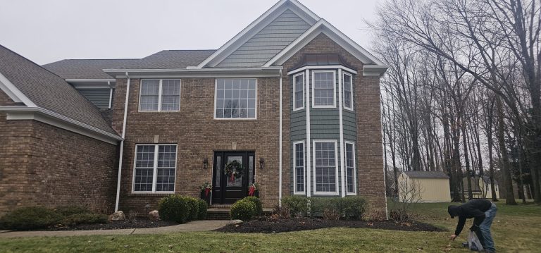 Split-level home with white siding, black shutters, and a blue front door, set on a grassy lawn with a brick foundation and autumn trees in the background.