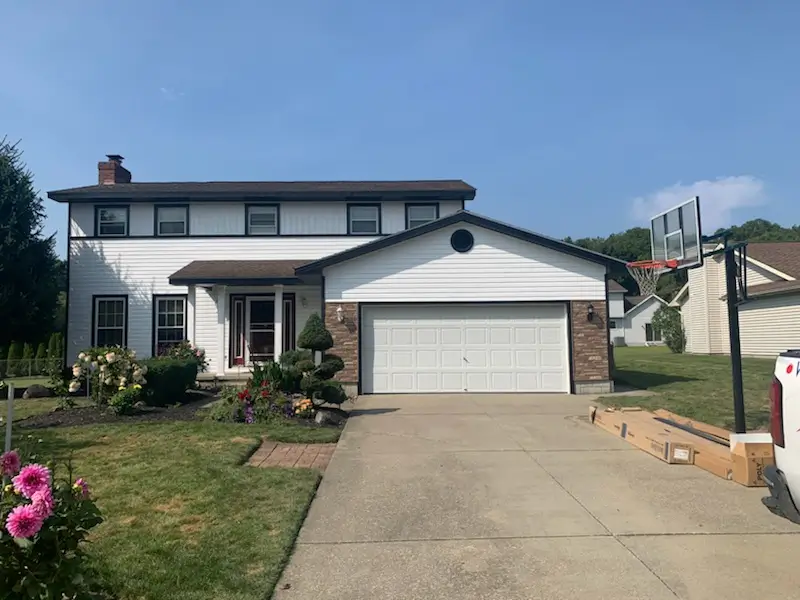 Split-level home with white siding, black shutters, and a blue front door, set on a grassy lawn with a brick foundation and autumn trees in the background.