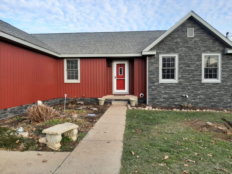 A red house with asphalt roofing, fresh mulch beds, and newly planted shrubs.