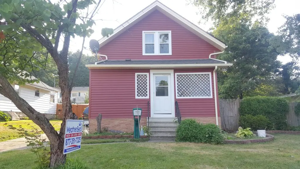 A red house with asphalt roofing, fresh mulch beds, and newly planted shrubs.