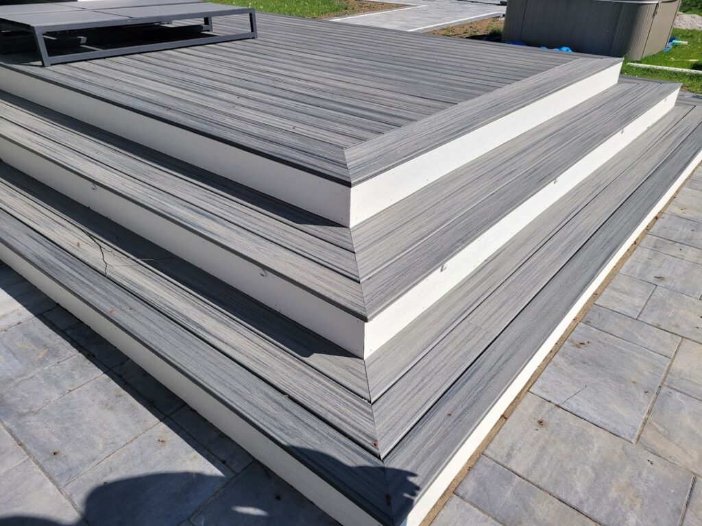 Close-up of corner stairs on a new composite deck. The deck boards are textured grey, and the vertical stair risers are solid white.