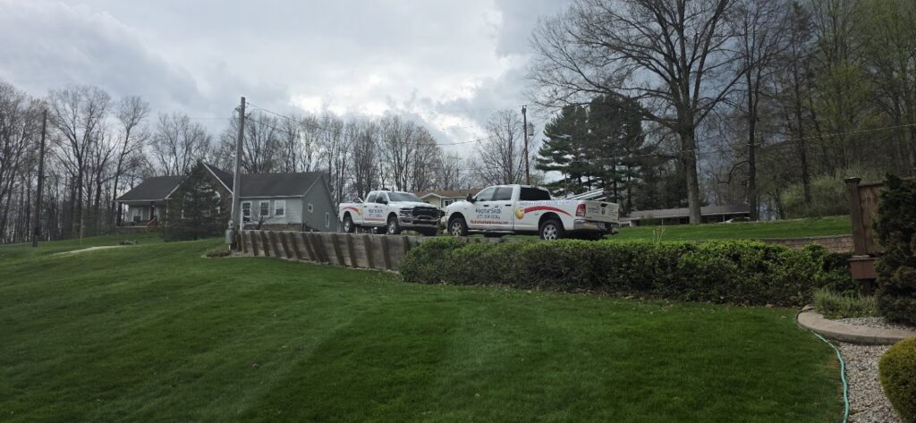 Two white WeatherSeal work trucks parked in a driveway next to a house on a grassy hill with a retaining wall in the front.